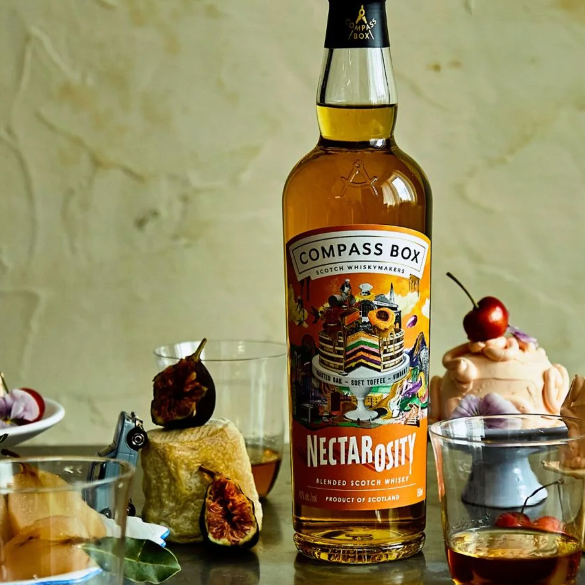 Bottle of Compass Box Nectarosity Blended Scotch Whiskey with vibrant label, surrounded by tasting glasses and garnishes.