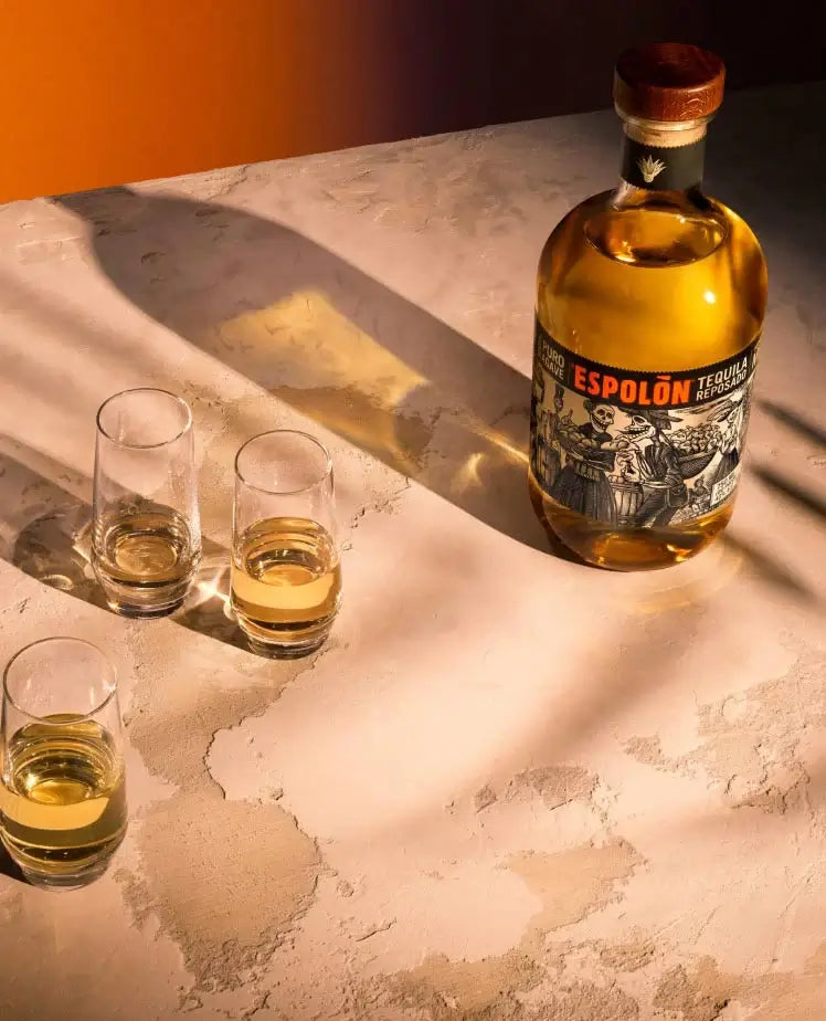 Espolòn Reposado Tequila bottle with shot glasses on a textured surface.