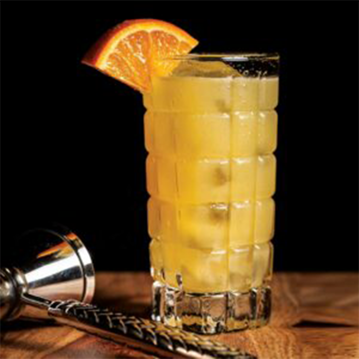 A refreshing cocktail in a tall glass with an orange slice garnish and ice, on a wooden bar top.
