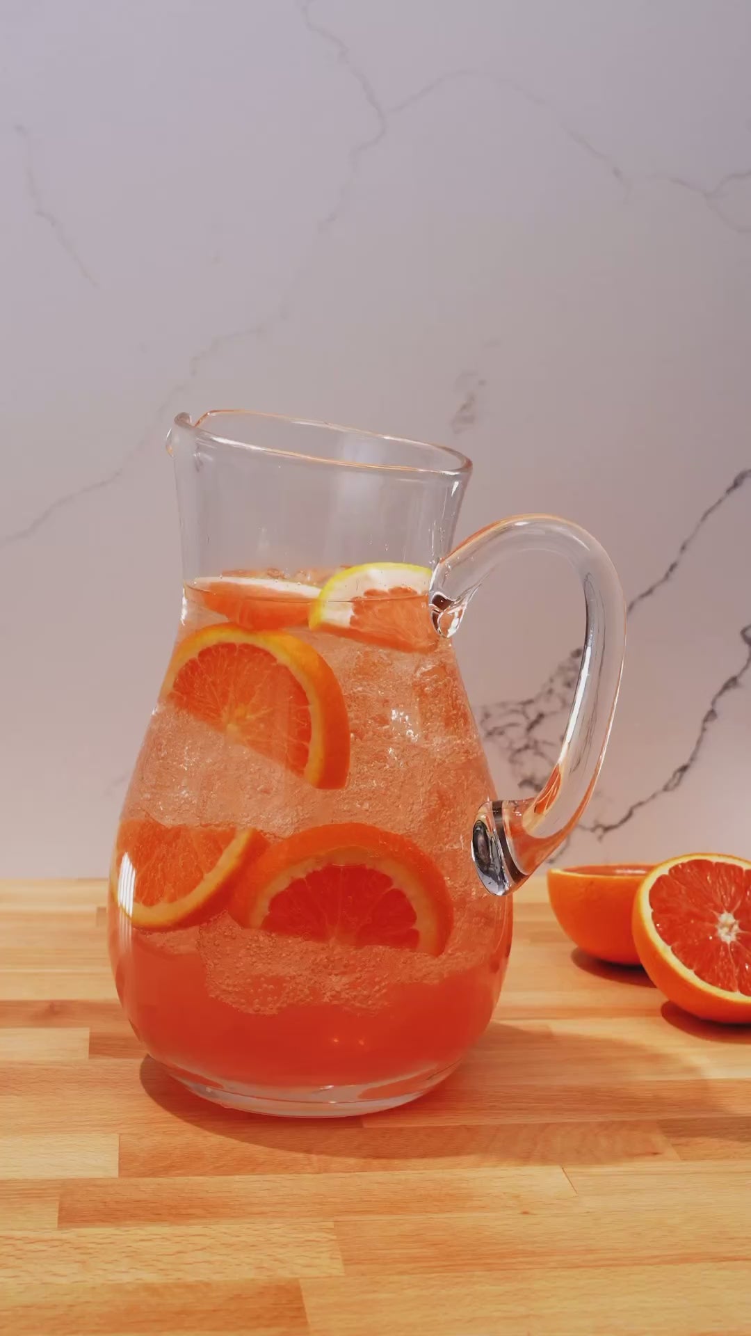 A clear pitcher filled with refreshing orange-infused beverage and slices of orange on a wooden table.