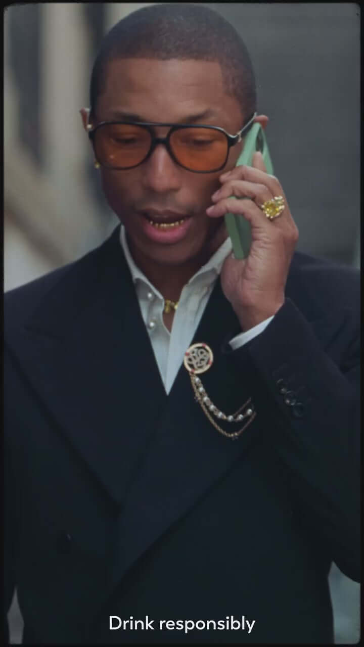 Pharrell Williams in a stylish outfit, talking on the phone, promoting responsible drinking.