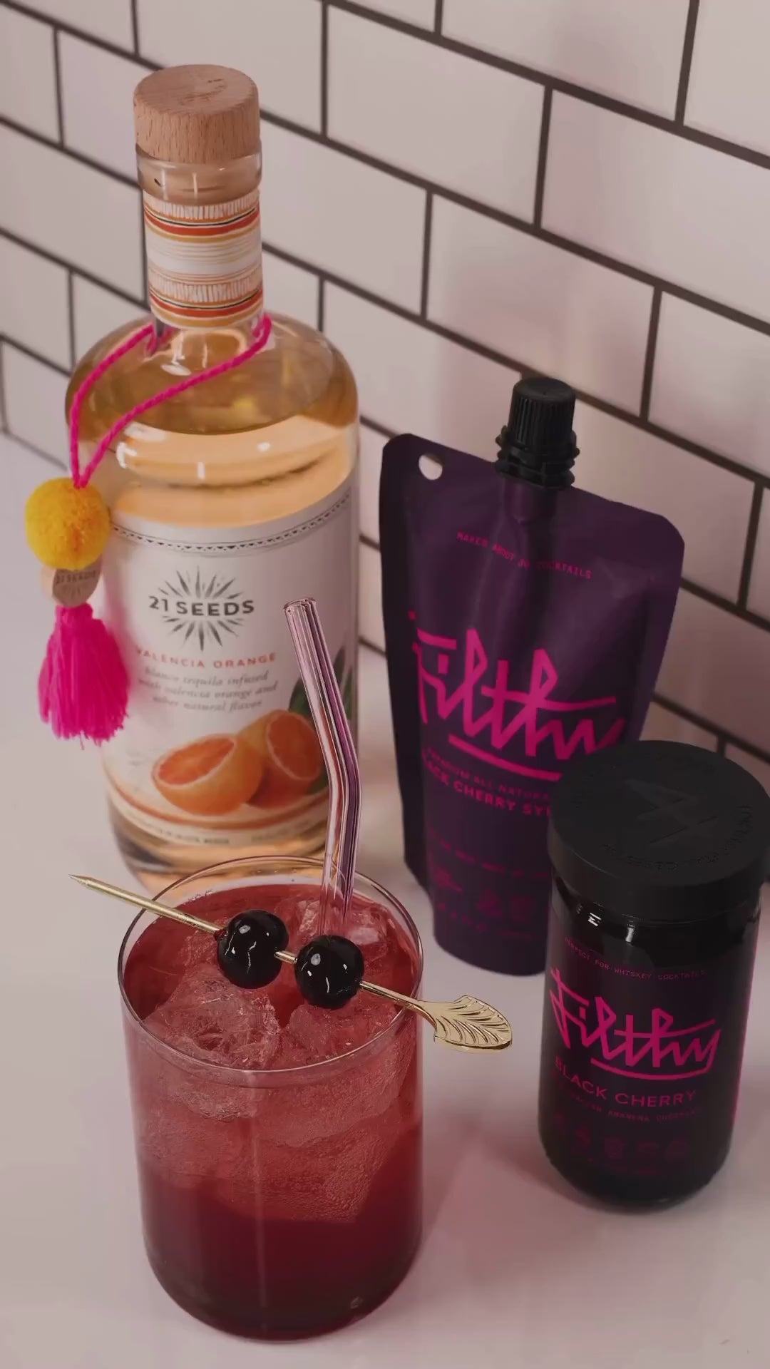 21 Seeds Valencia Orange tequila bottle with cocktail, garnished with cherries, alongside Filthy mix products.