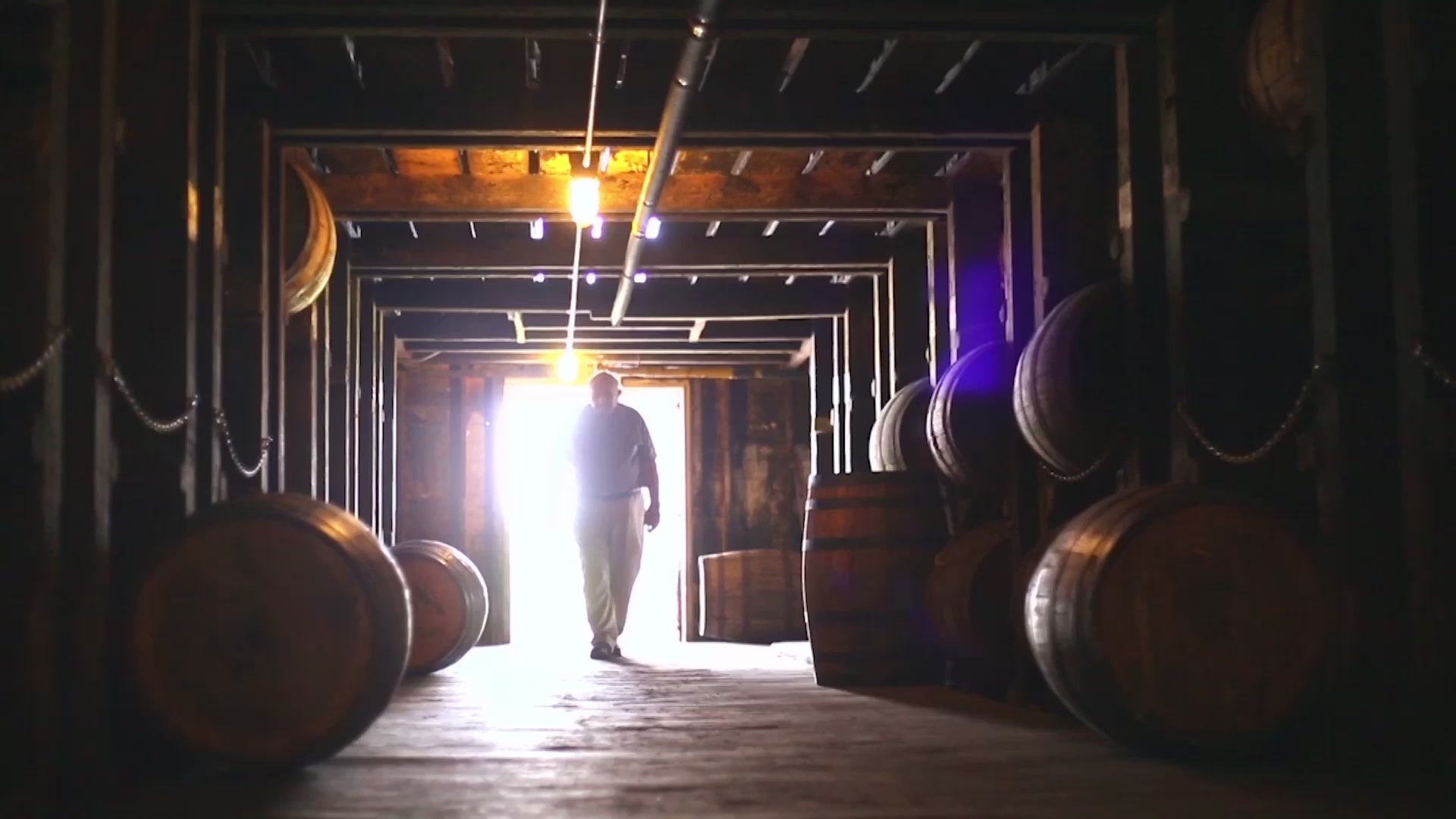 A silhouetted figure walking through a bourbon barrel storage room, highlighting the bourbon aging process.