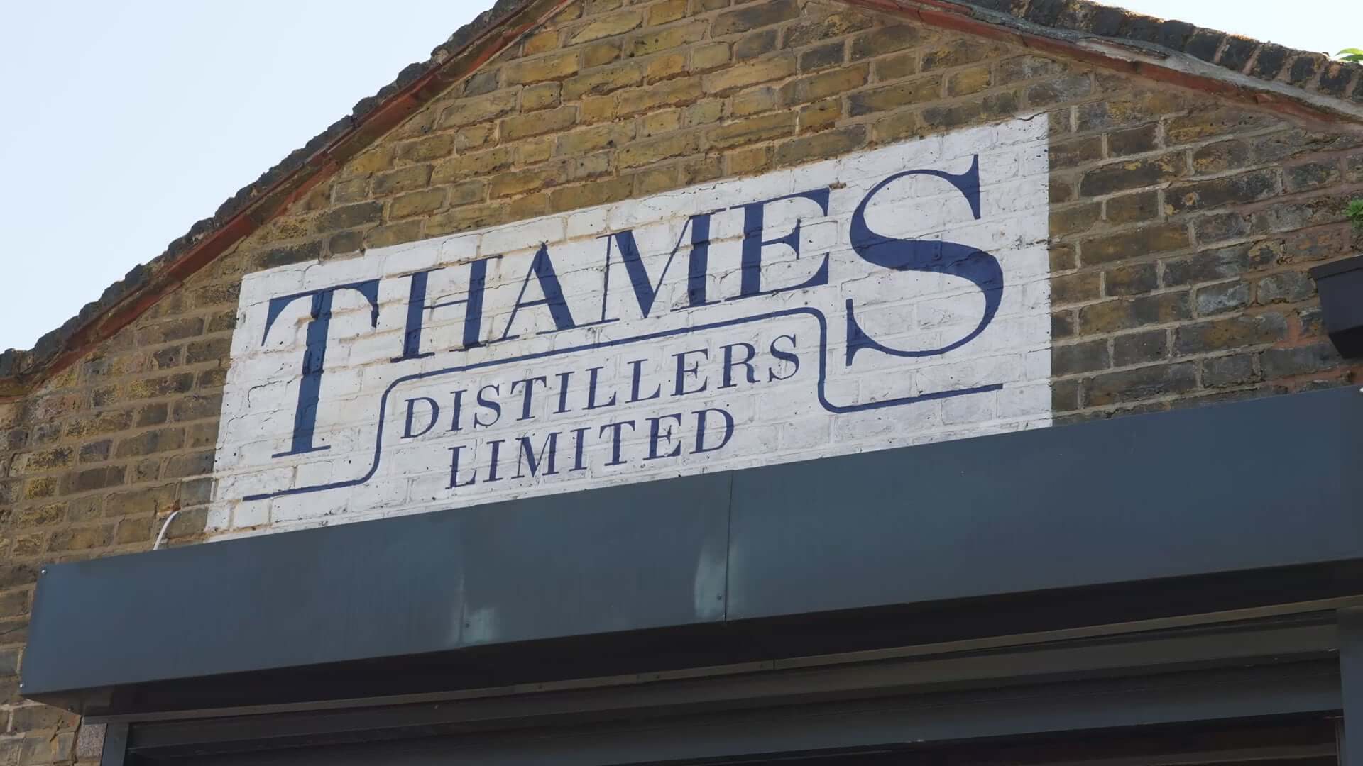 Sign of Thames Distillers Limited on a brick wall, showcasing artisanal distilling craftsmanship.