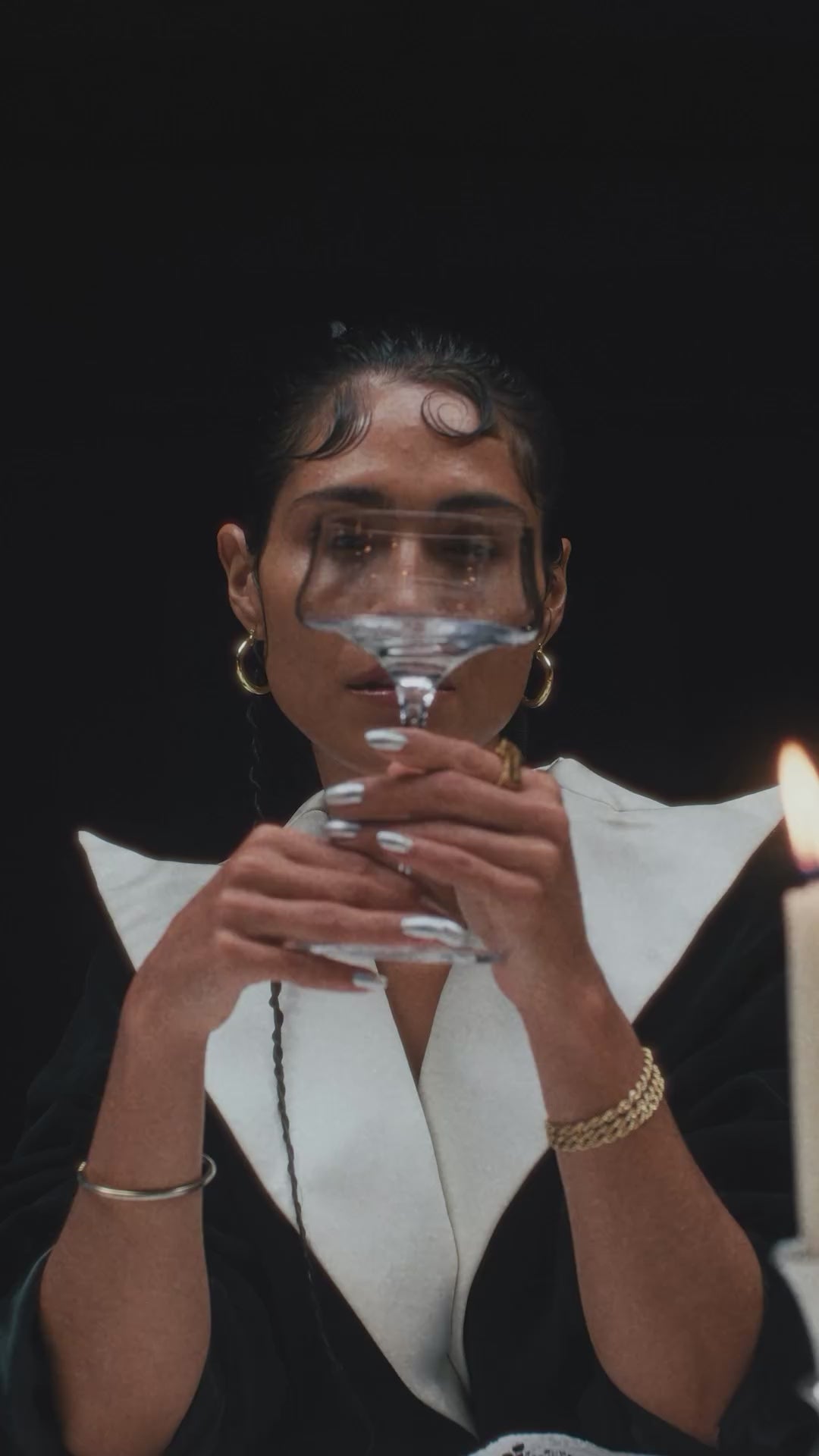 Woman holding a crystal glass with a candle in the background, showcasing modern elegance and style.