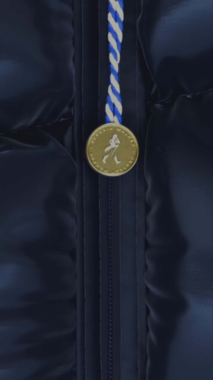 Close-up of a gold emblem on a navy puffer jacket zipper, showcasing luxury ski wear design.