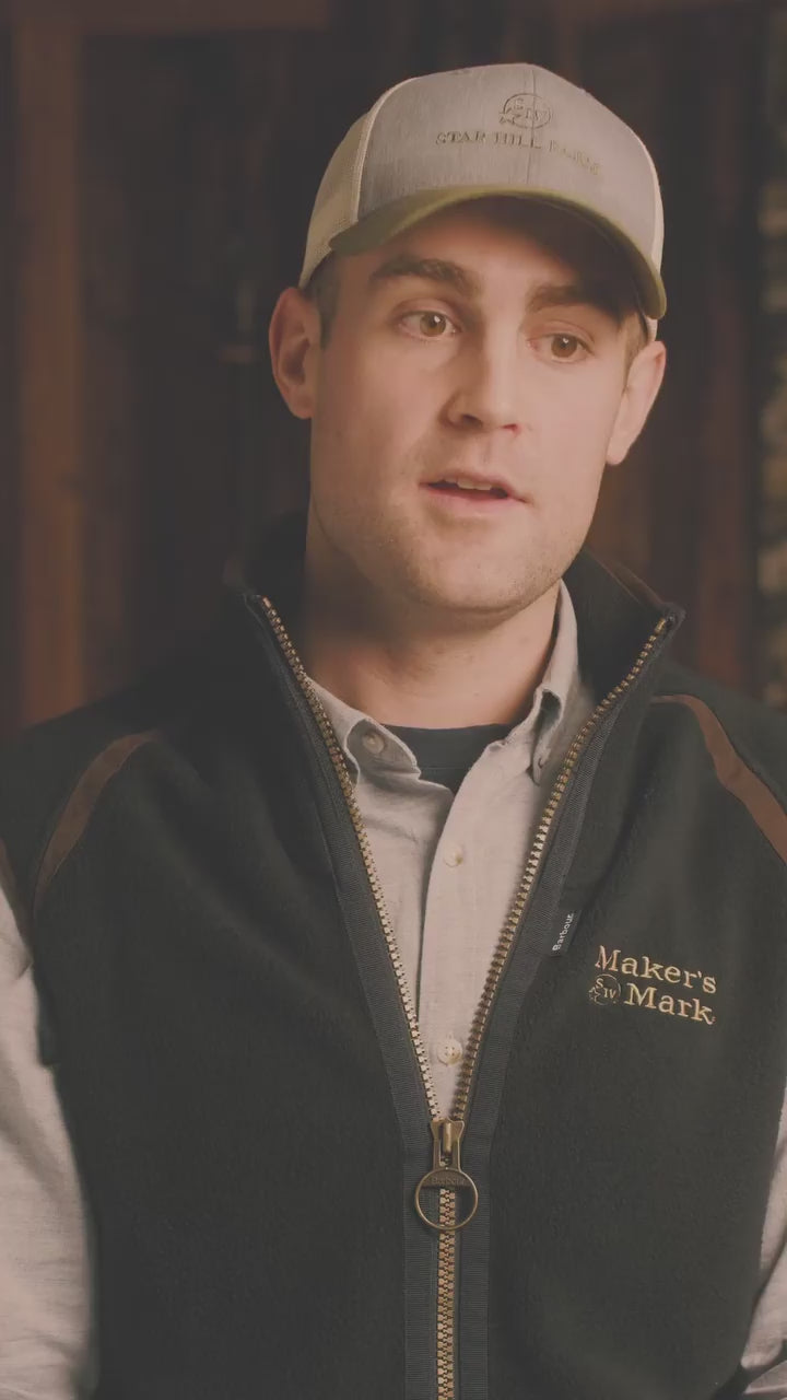Young man wearing a Maker's Mark vest and cap, sharing insights about the bourbon distilling process.