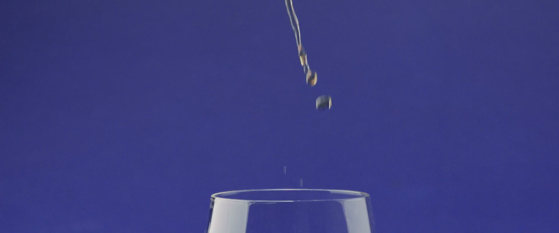 Droplets falling into a glass against a vibrant blue background, evoking the enjoyment of whiskey tasting.