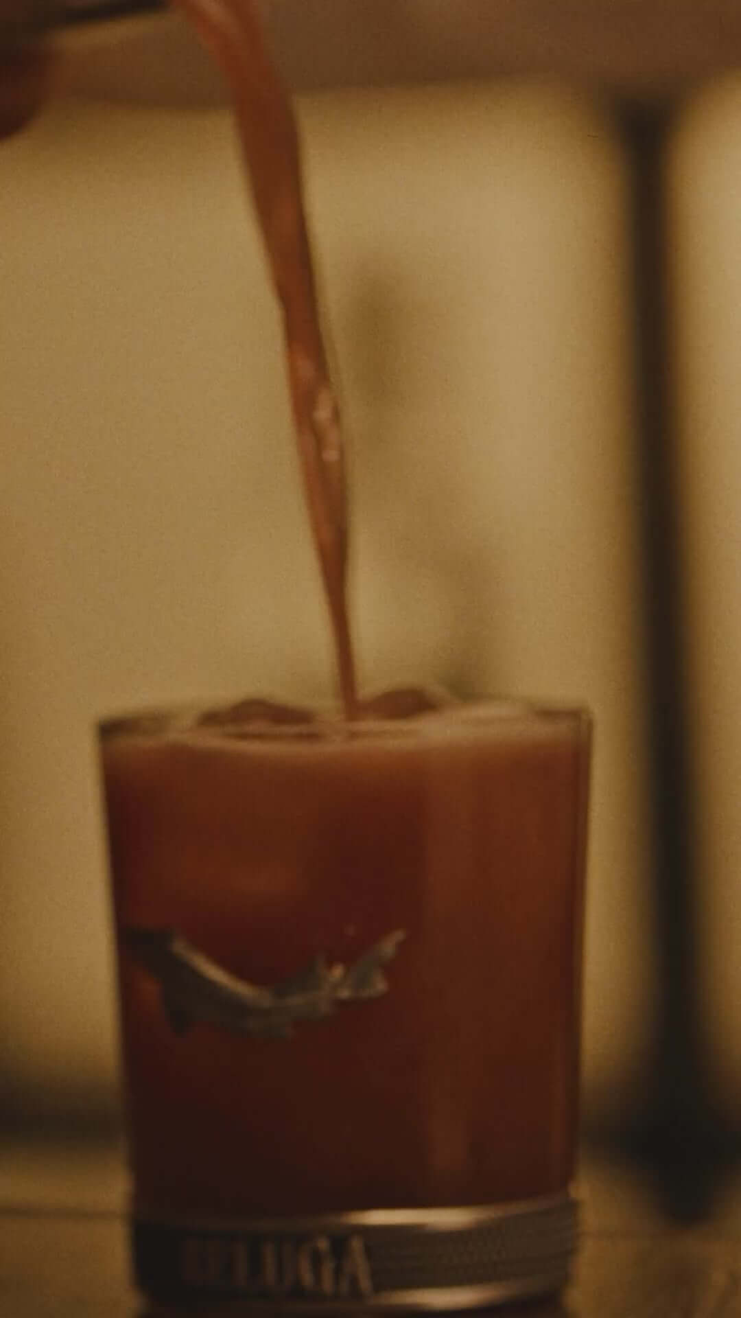 Pouring a cocktail into a glass with a Beluga logo, showcasing the richness of Beluga Gold Line vodka.