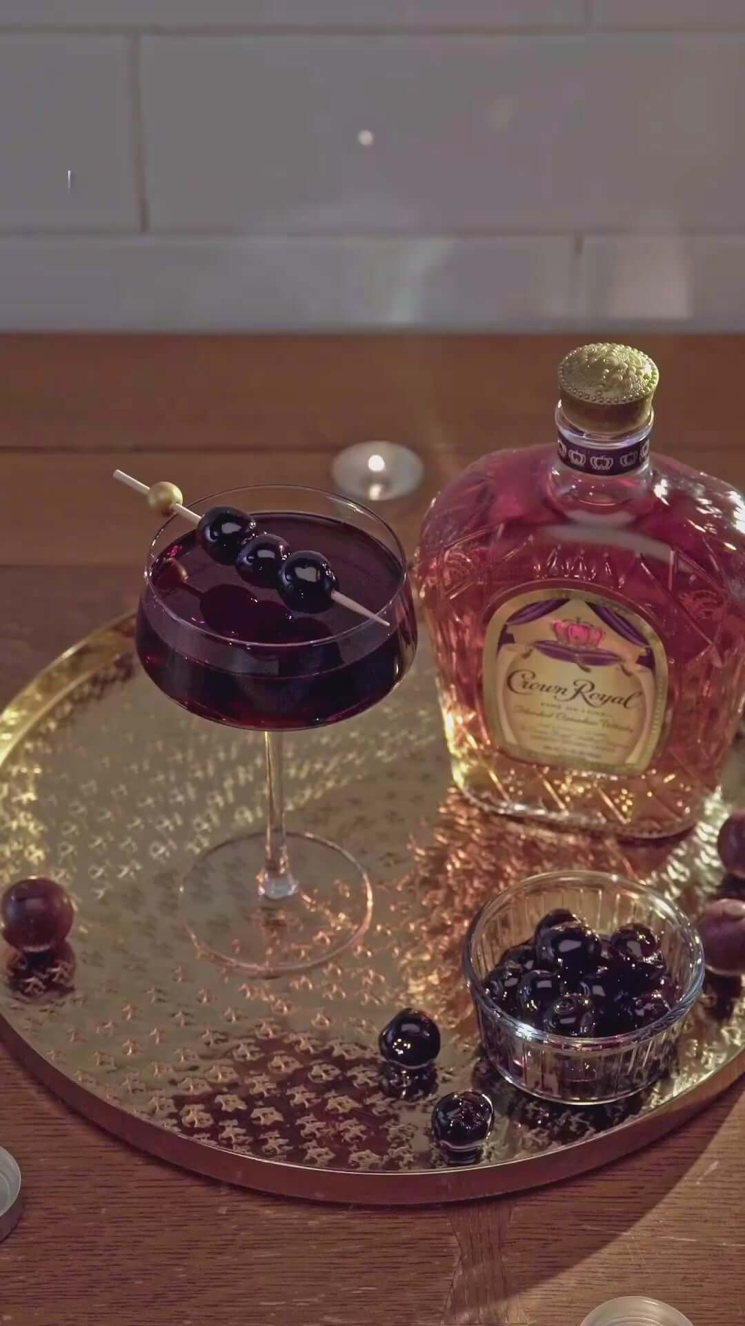 Crown Royal Canadian Whisky displayed with a cocktail and fresh cherries on a golden tray.
