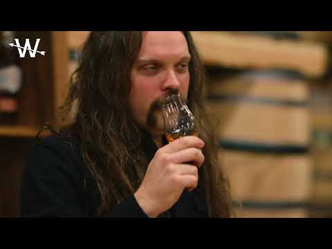 Man savoring a glass of Westward American Single Malt whiskey in a rustic distillery setting.