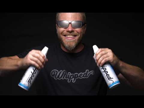 Man in sunglasses holding two cans of Lick the Whip So Vanilla alcohol-infused whipped cream, smiling and ready to serve.