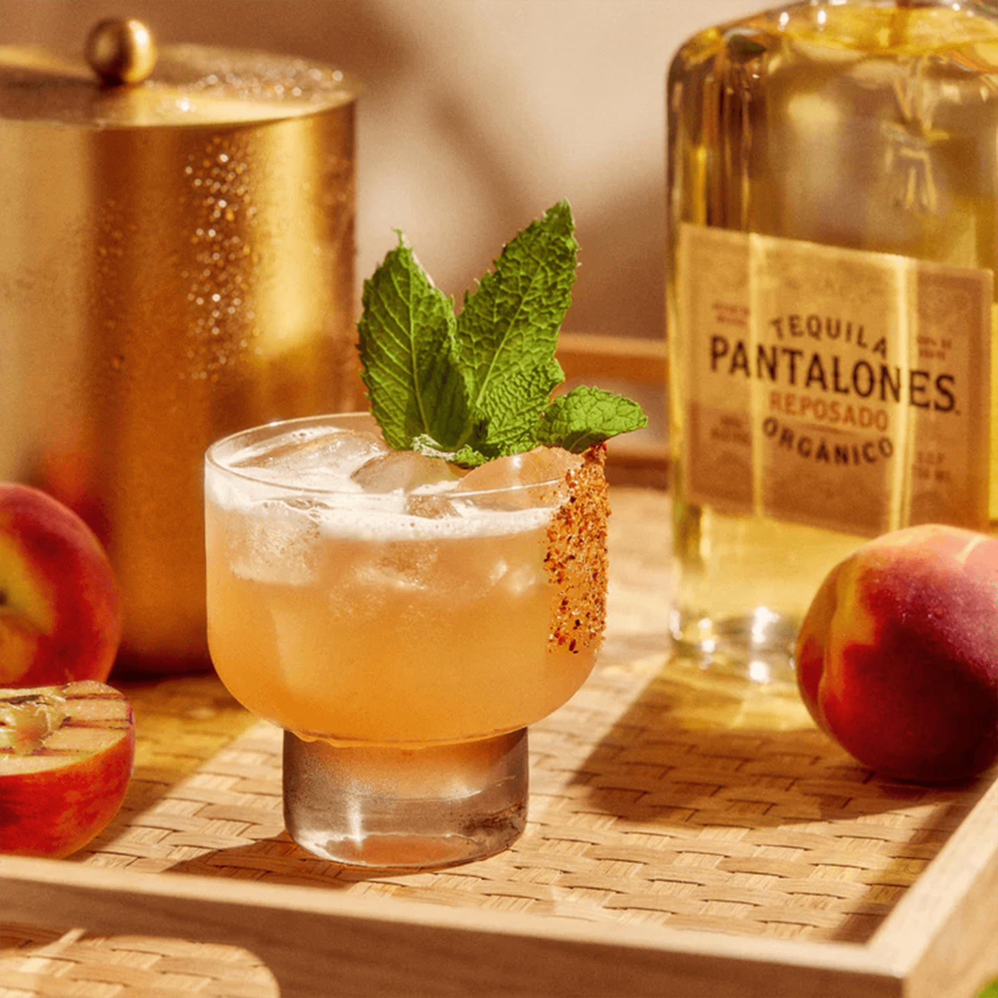 Refreshing cocktail with mint, served in a glass next to Pantalones Reposado Tequila and fresh peaches.