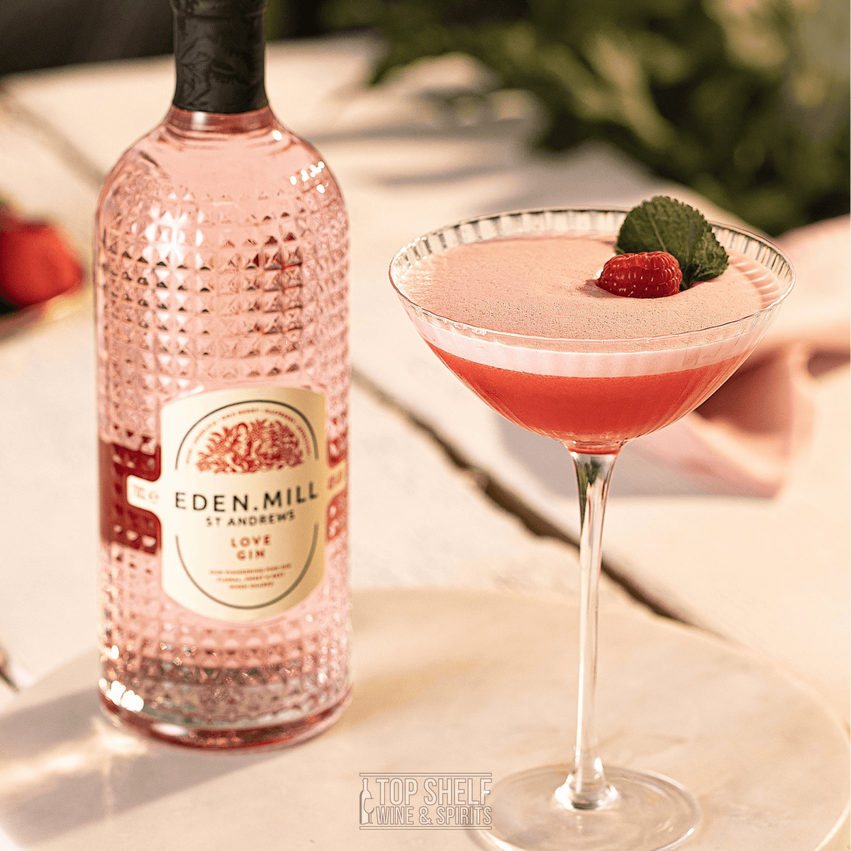 Eden Mill St Andrews Love Gin bottle with a beautifully garnished cocktail, featuring raspberries and mint.