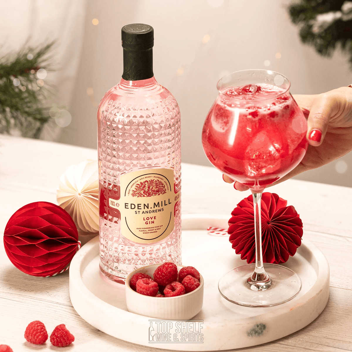 Eden Mill St Andrews Love Gin 700ml displayed with a cocktail and fresh raspberries, showcasing its pink color and festive appeal.