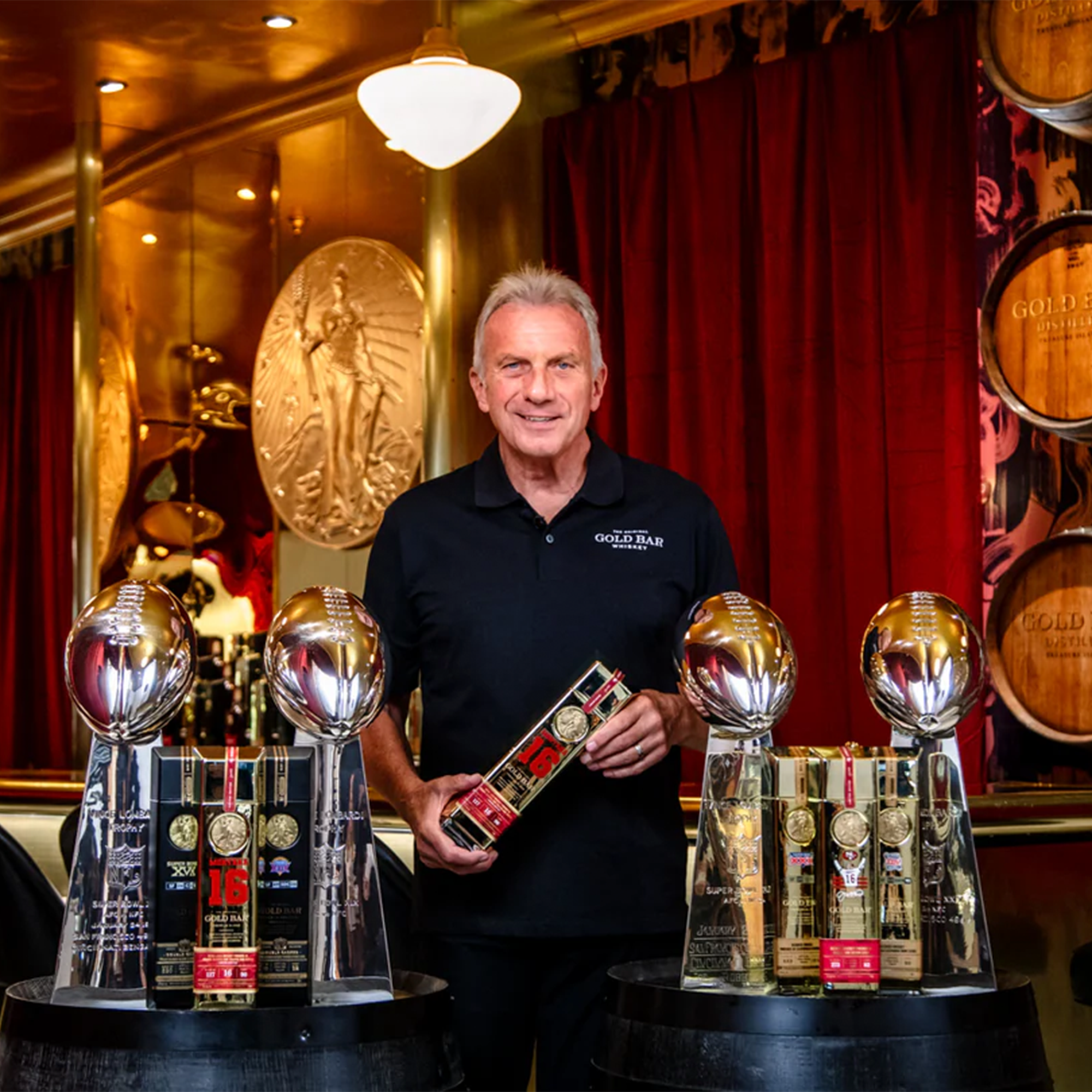 Joe Montana presenting the Gold Bar Championship Collection Whiskey Set with Super Bowl trophies in a luxurious setting.