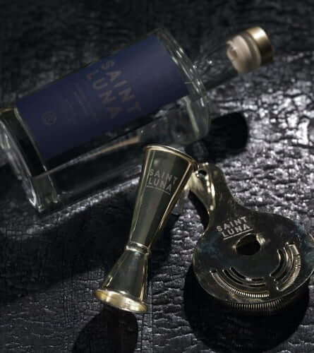 Saint Luna Charcoal Filtered Moonshine bottle with jigger and strainer, showcasing sophistication in mixology.