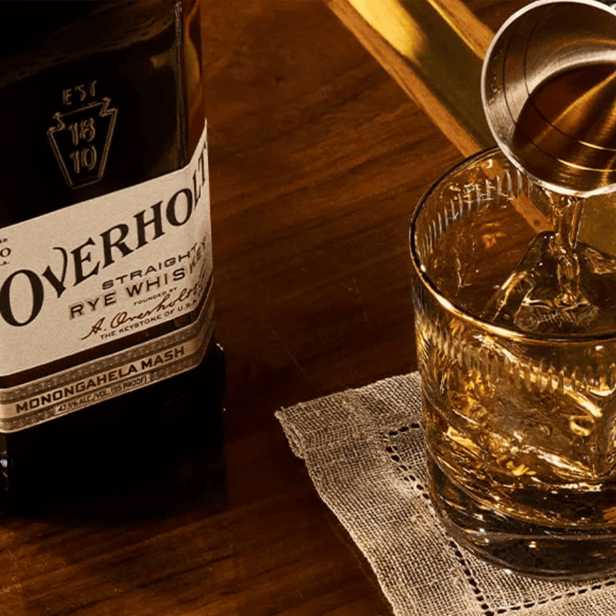 A. Overholt 4 Year Rye Whiskey bottle next to a glass filled with whiskey, showcasing Monongahela Mash heritage.