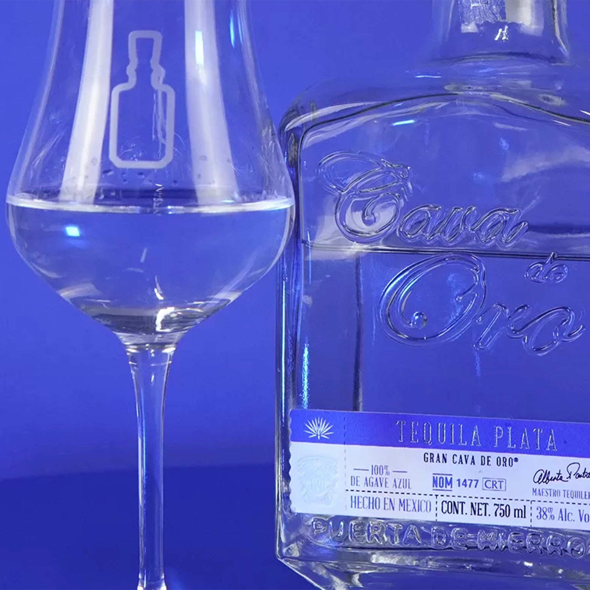 Cava De Oro Plata Tequila bottle beside a tasting glass, highlighting its clear, luminous color and branding.