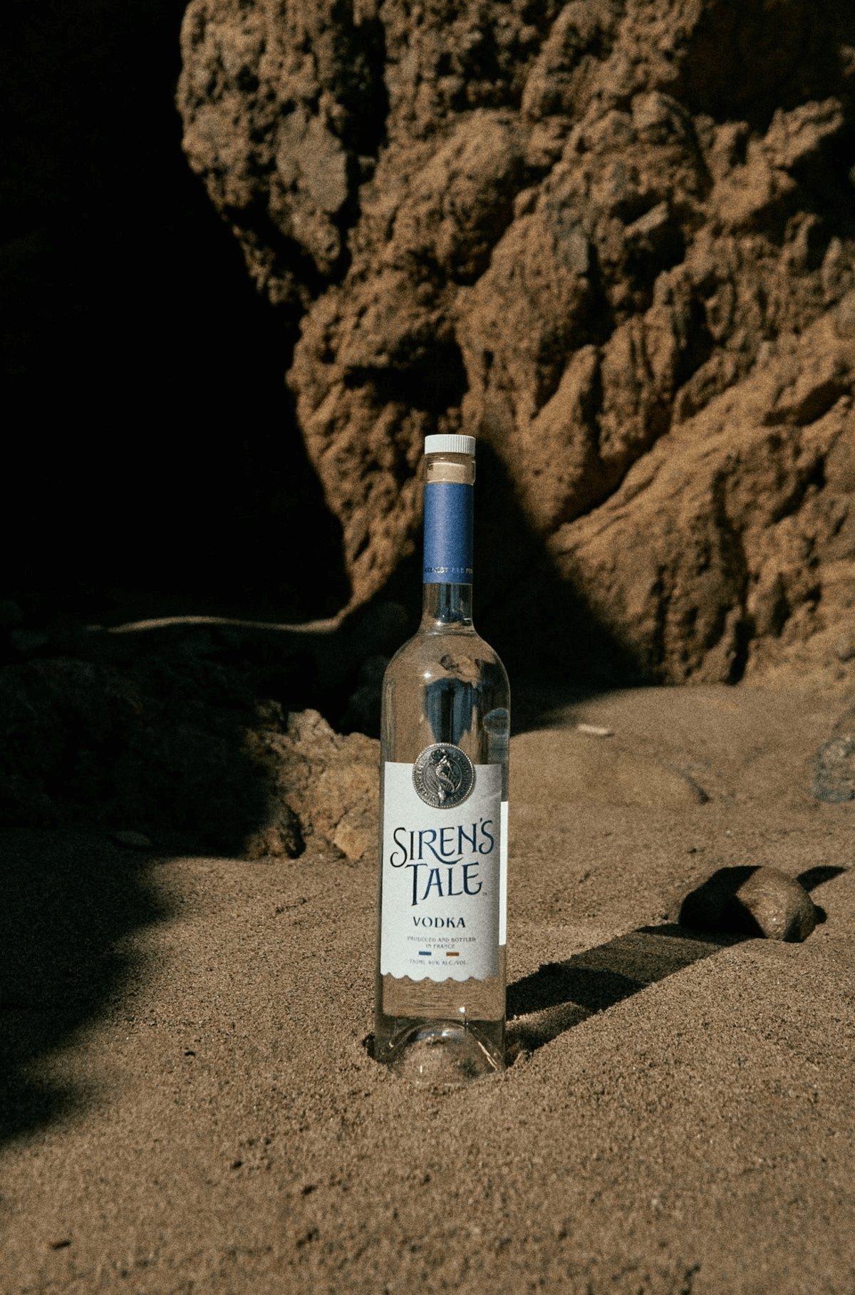 Siren's Tale French Vodka bottle on sandy beach, showcasing its elegance and quality.