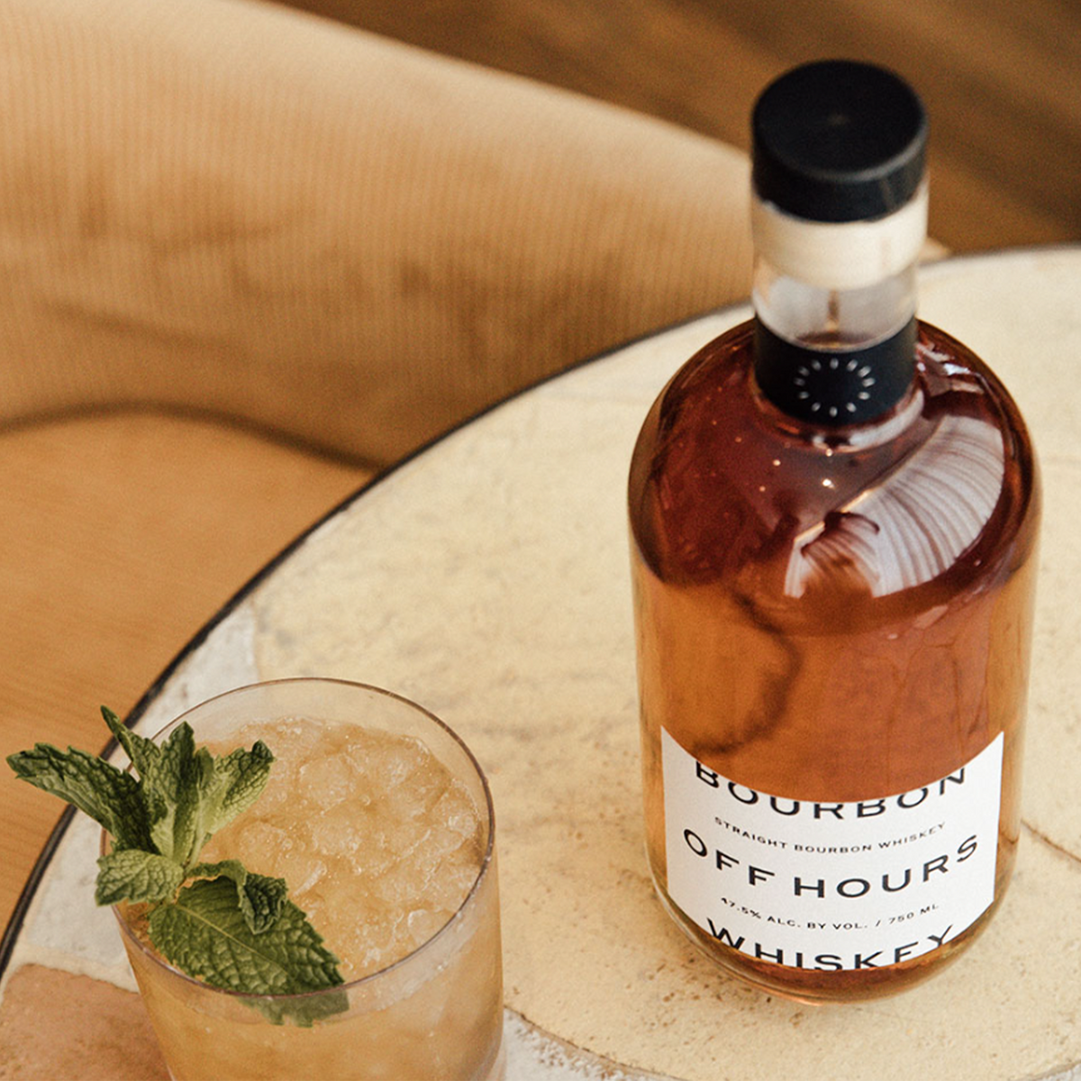 Off Hours Single Barrel Bourbon bottle with a cocktail garnished with mint on a rustic table.