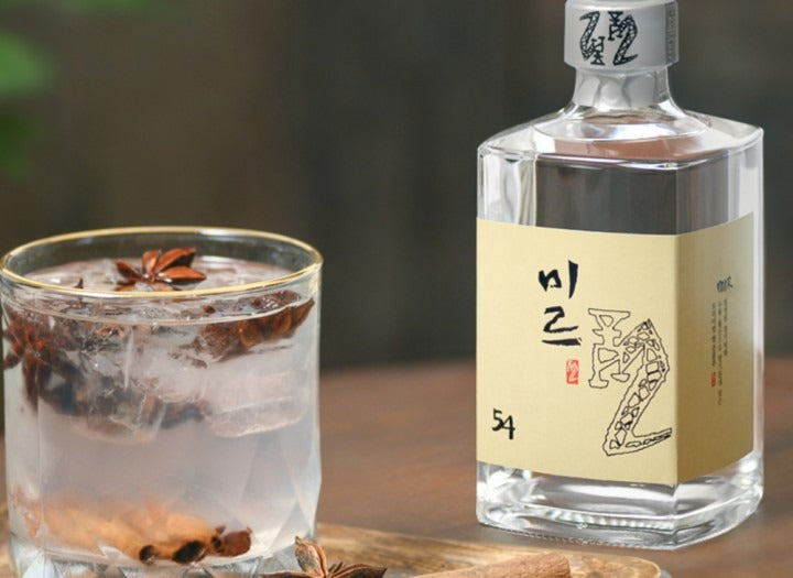 Bottle of Sulseam Mir 22 Soju 375mL beside a glass of cold soju with ice and garnishes on a wooden table.