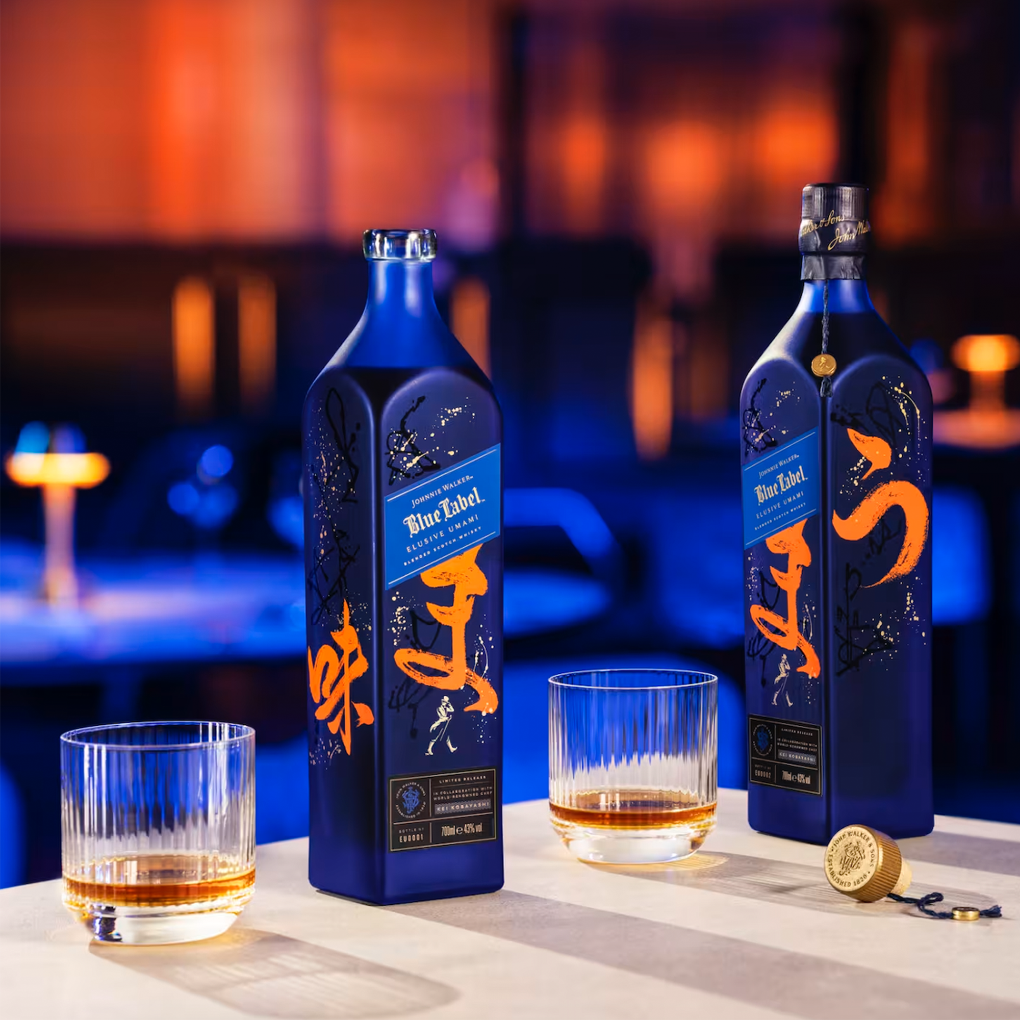 Johnnie Walker Blue Label Umami Scotch bottle and glasses on a bar table, showcasing a limited edition design.