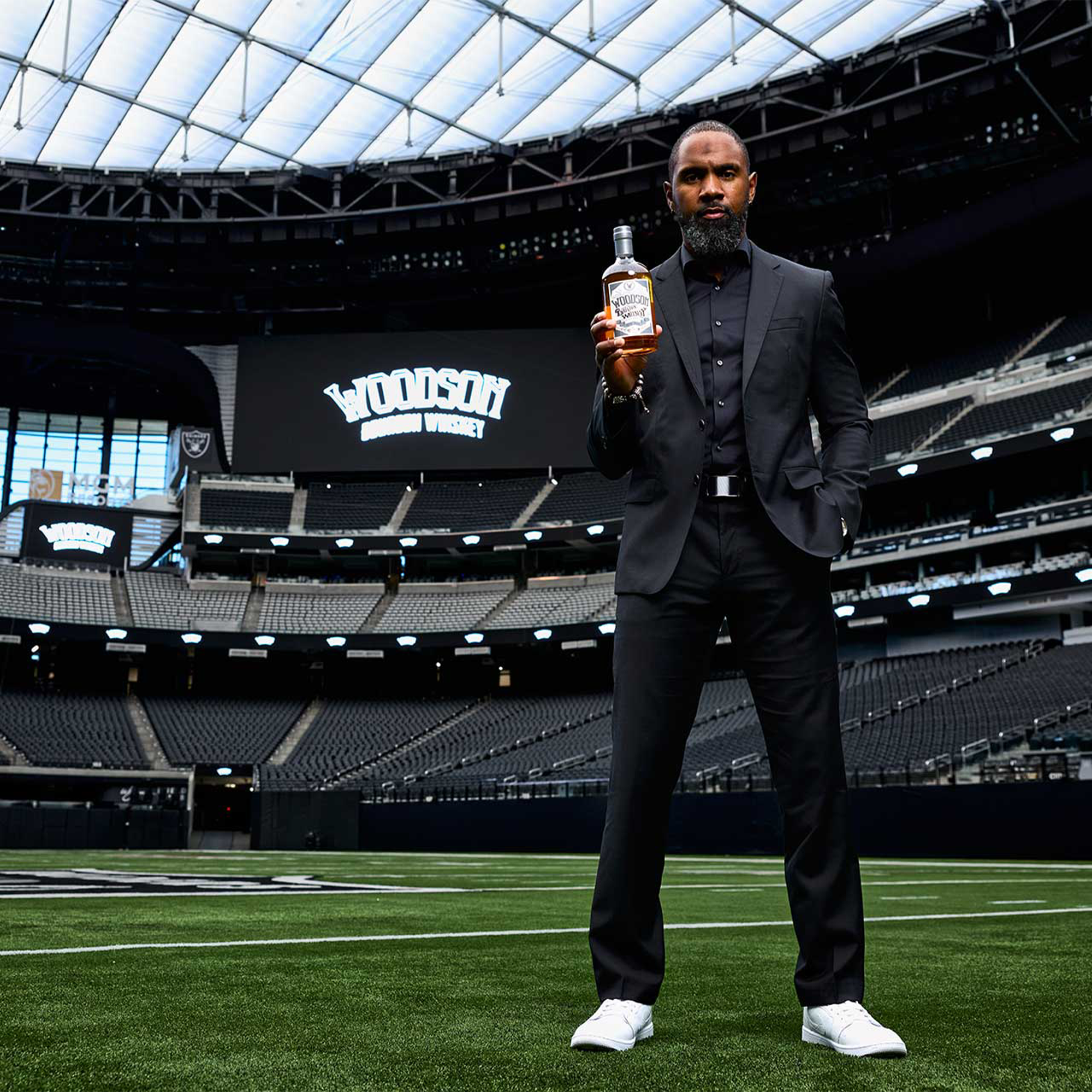 Man in a suit holding Woodson bourbon at a stadium, showcasing the limited edition bottle.