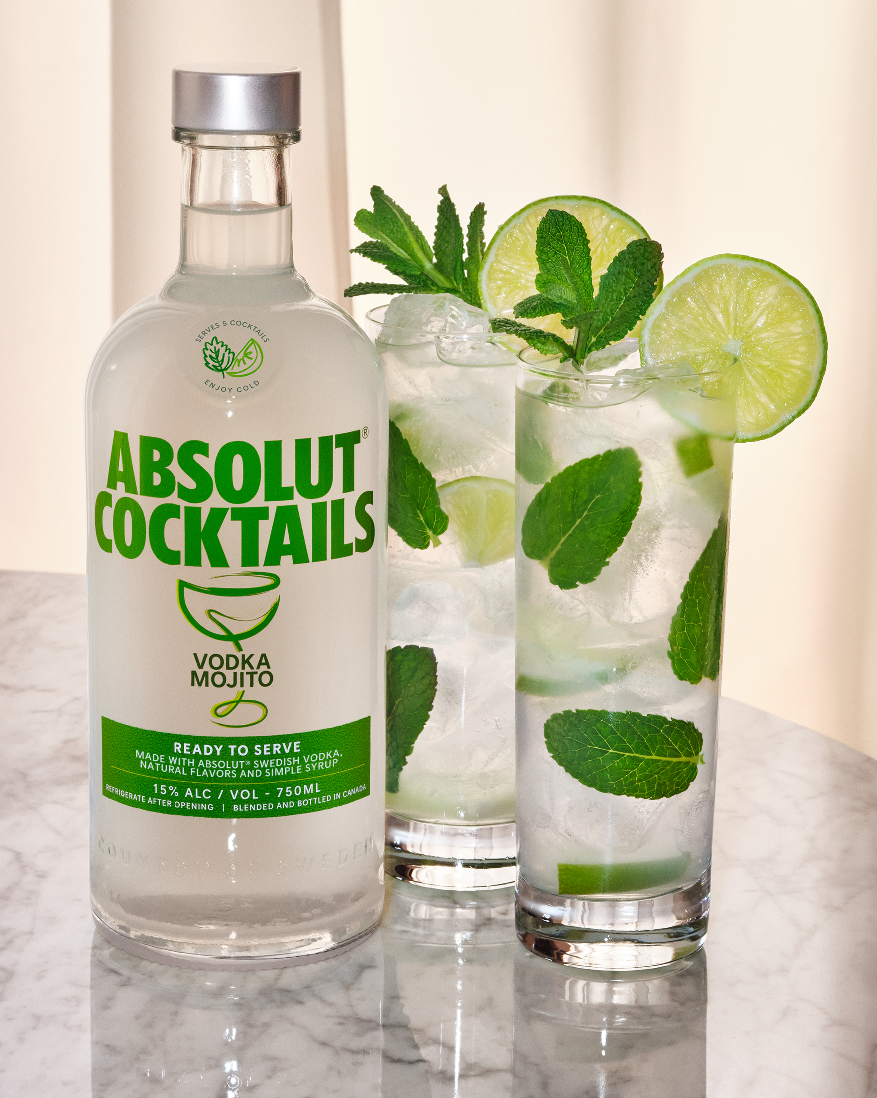 Absolut Mojito Vodka bottle next to refreshing mint mojito cocktails with lime and mint garnish.