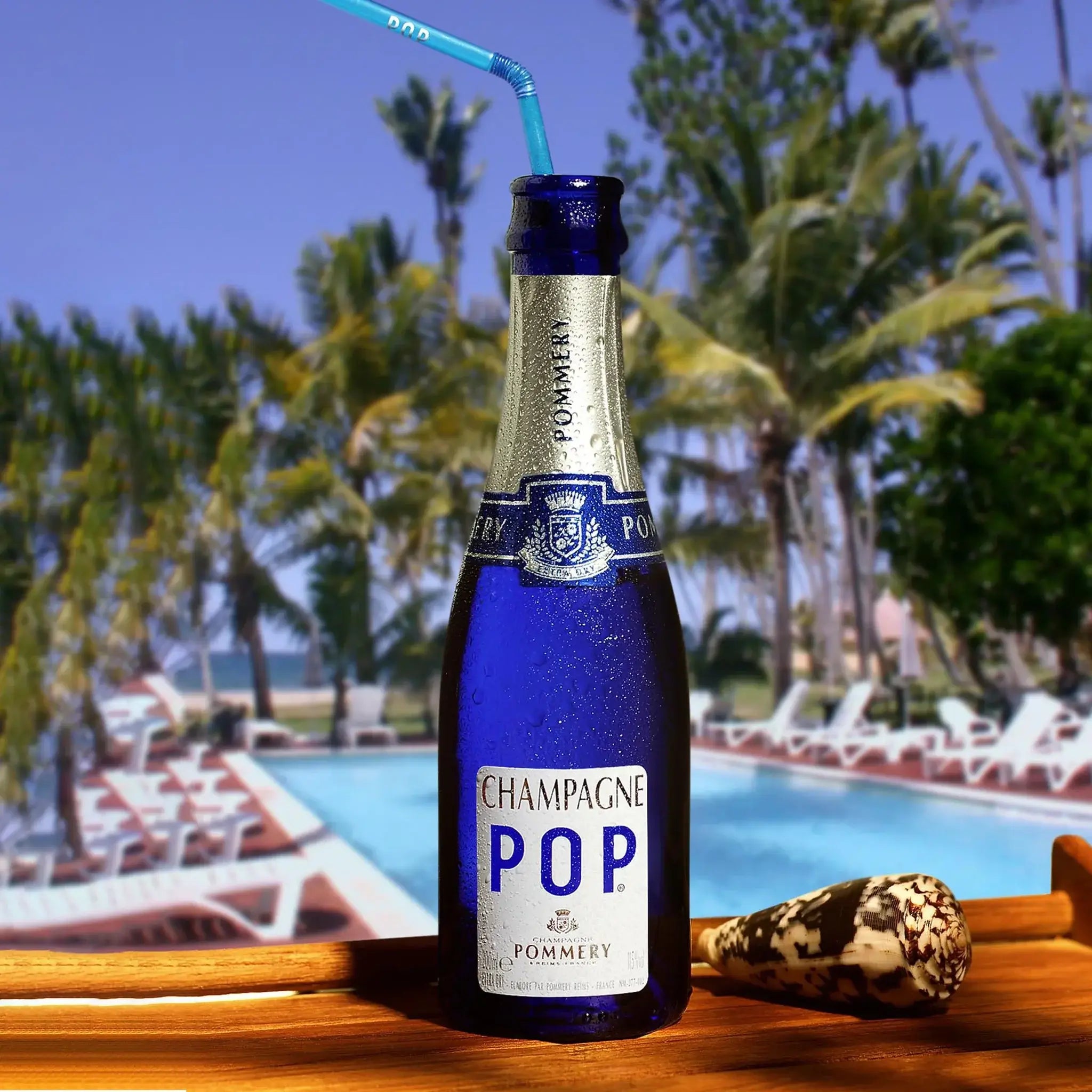Pommery Pop Extra Dry Champagne 187mL with straw, poolside in a tropical setting, perfect for celebration.