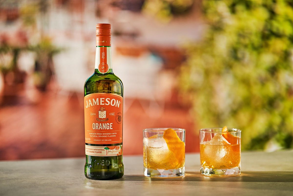 Jameson Orange Irish Whiskey bottle with two glasses of whiskey on ice and orange garnish in a vibrant setting.