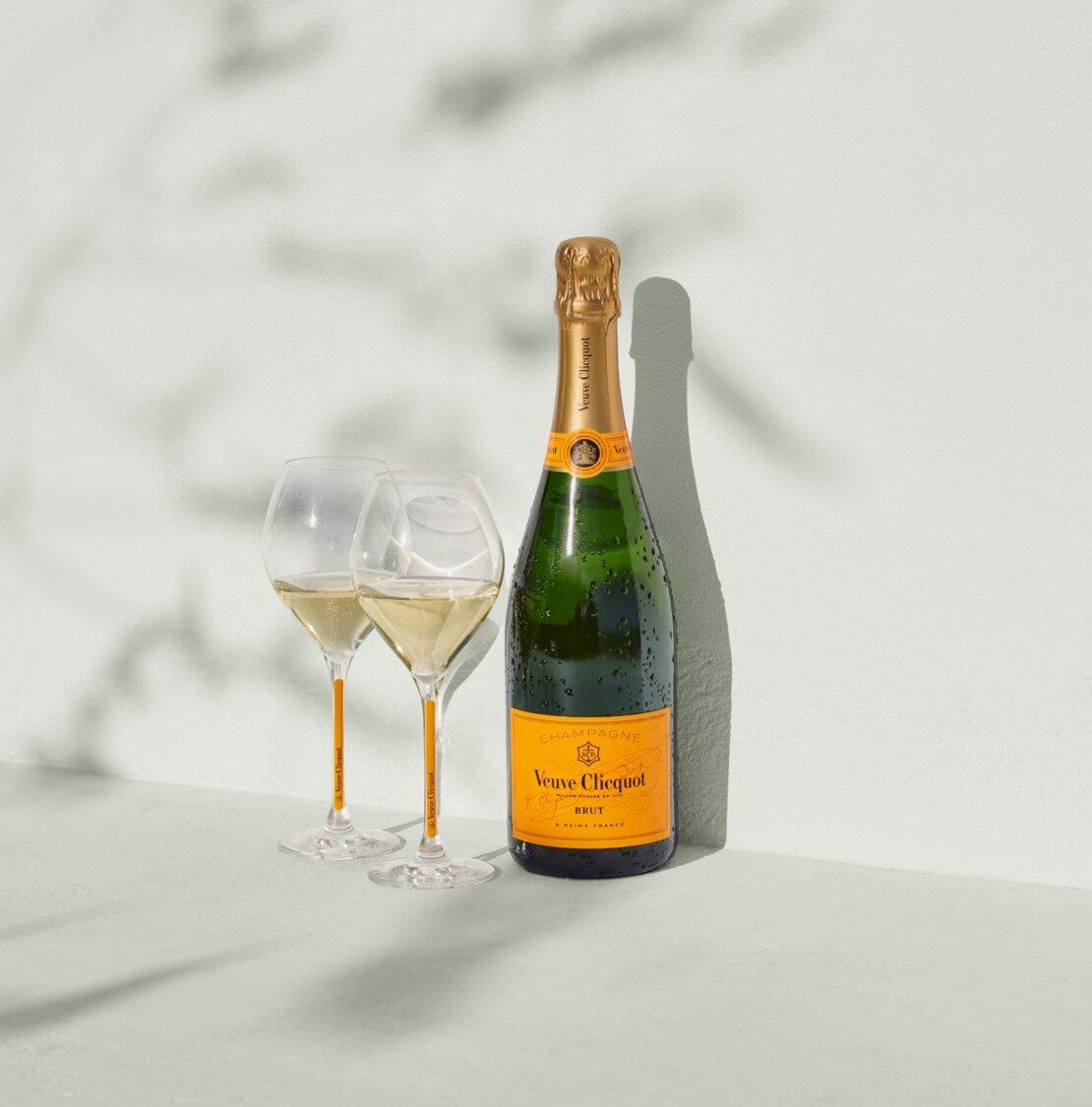 Veuve Clicquot Brut Champagne bottle with two glasses on a light background, showcasing elegance and quality.