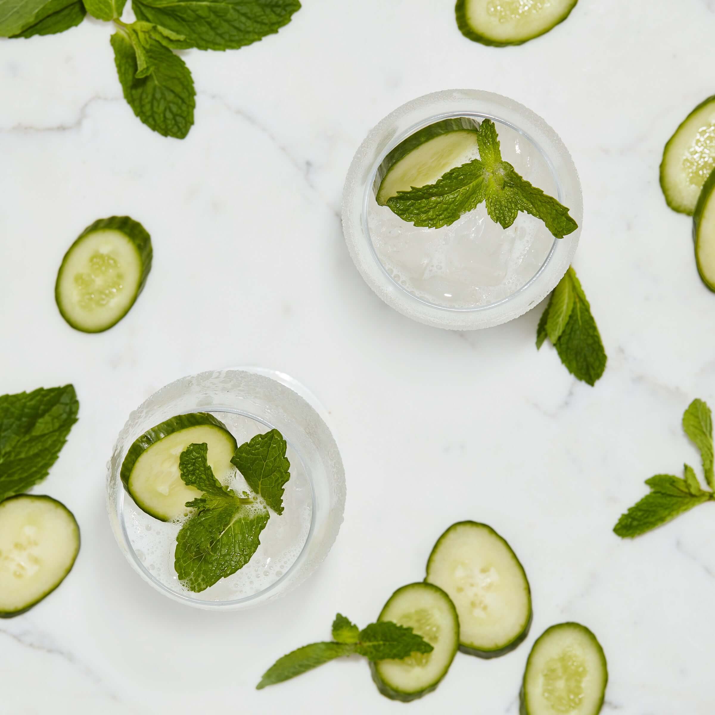 Refreshing cucumber and mint cocktails garnished with fresh mint leaves and cucumber slices on a marble surface.