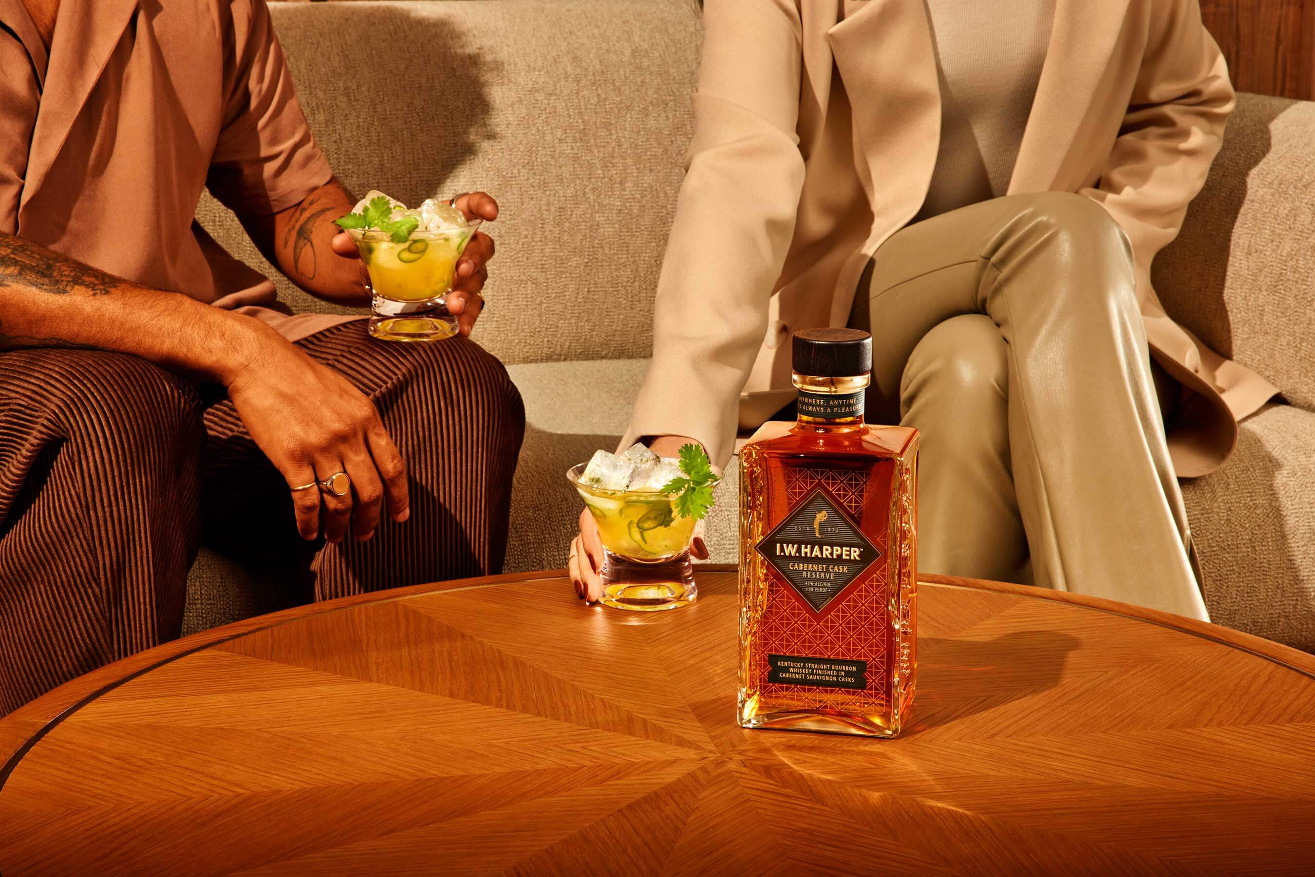 I.W. Harper Cabernet Cask Reserve bourbon on table with cocktails and two people enjoying drinks.