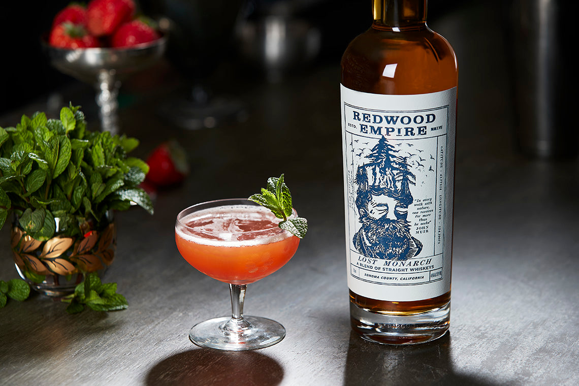 Redwood Empire Lost Monarch whiskey bottle with a cocktail garnished with mint in an upscale bar setting.