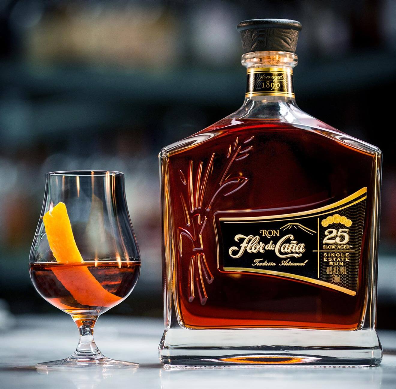 Ron Flor de Caña 25 year Rum bottle next to a glass with a drink and orange twist.