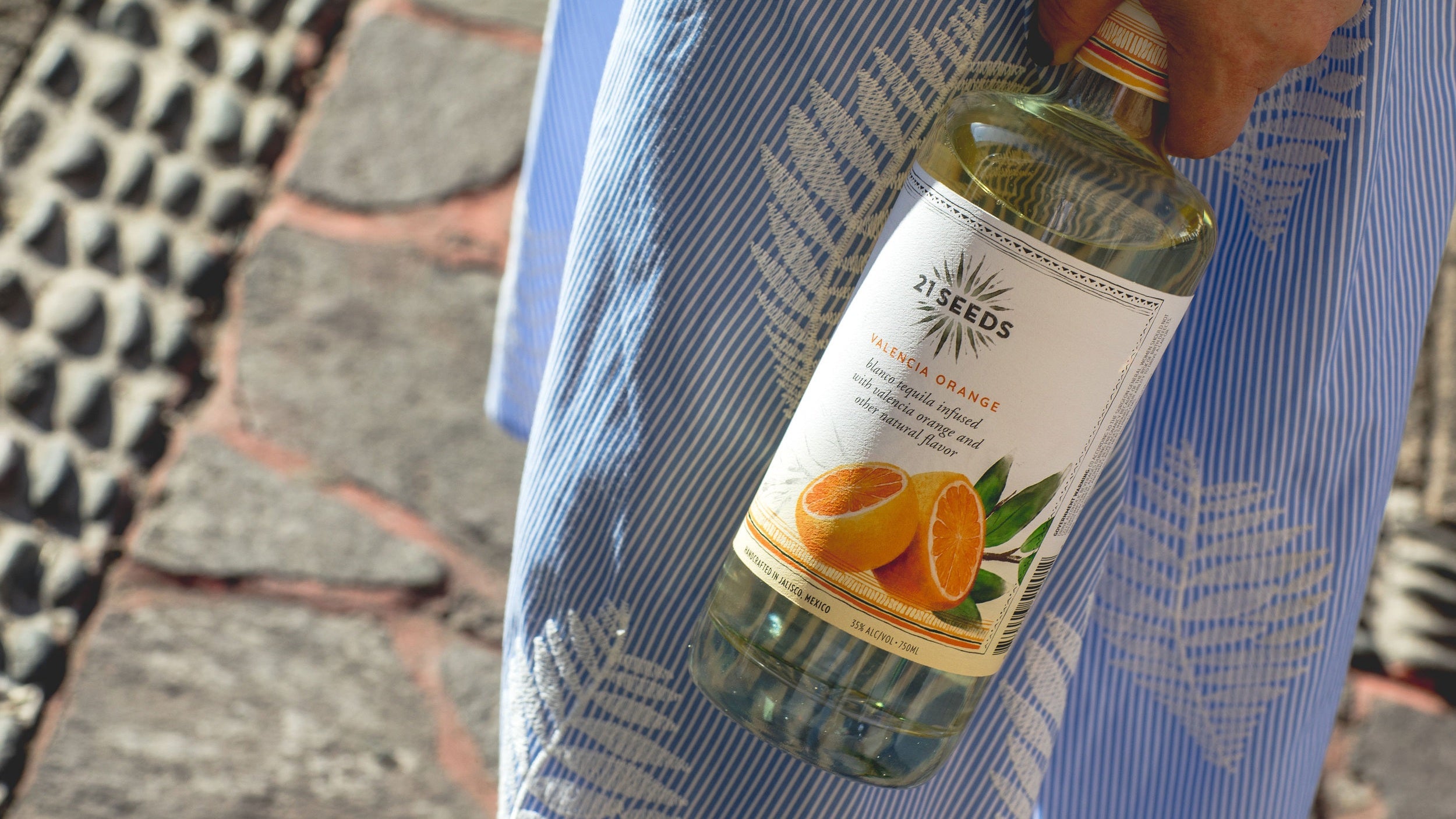 21Seeds Valencia Orange Tequila bottle held in hand, featuring bright orange notes for refreshing summer cocktails.