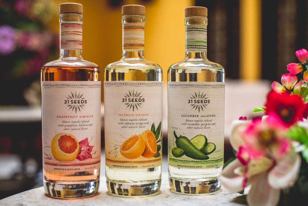 Three bottles of 21 Seeds tequila: Grapefruit Hibiscus, Valencia Orange, and Cucumber Jalapeño on a table.