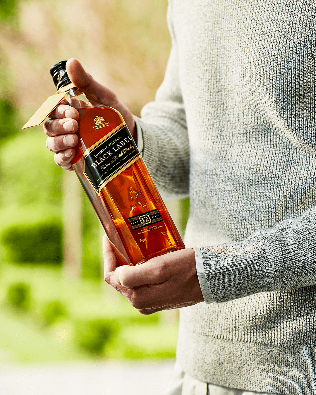Person holding a bottle of Johnnie Walker Black Label whisky, showcasing its rich amber color and iconic label.