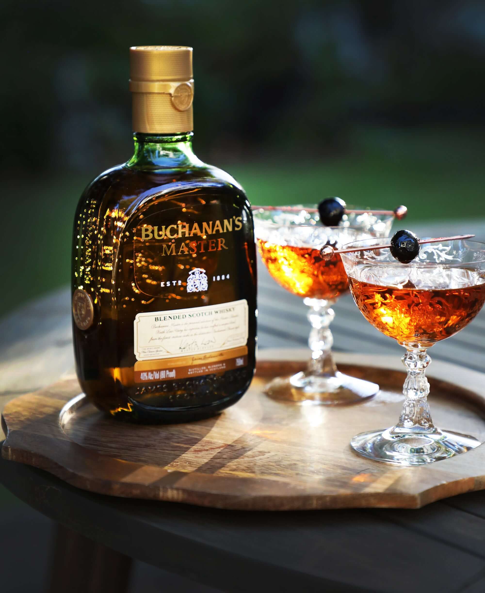 Buchanan's Master Whisky bottle with two cocktails on a wooden tray, perfect for enjoying its herbal and citrus flavors.
