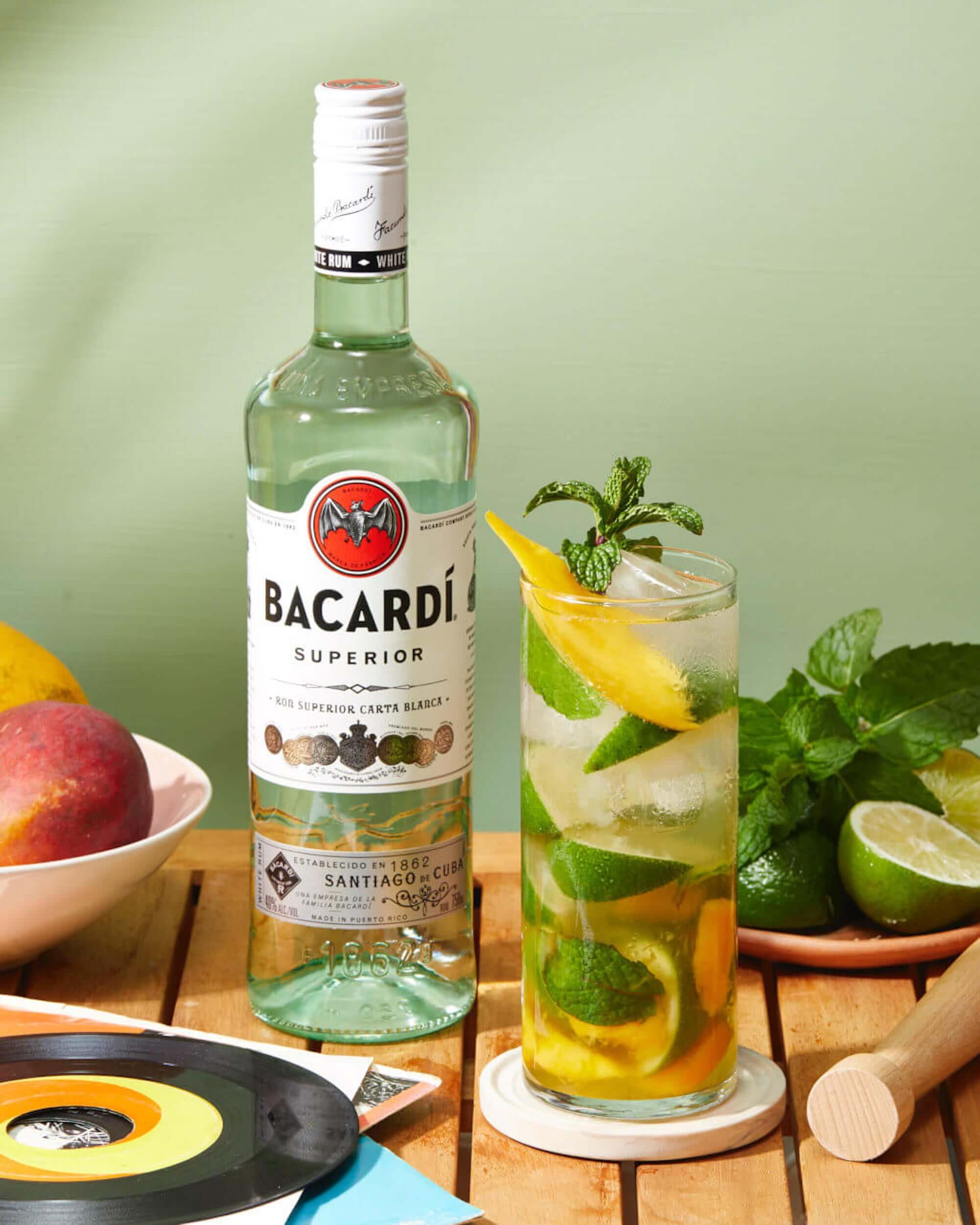 BACARDÍ Superior Rum bottle next to a refreshing Mojito cocktail with mint and citrus on a wooden table.