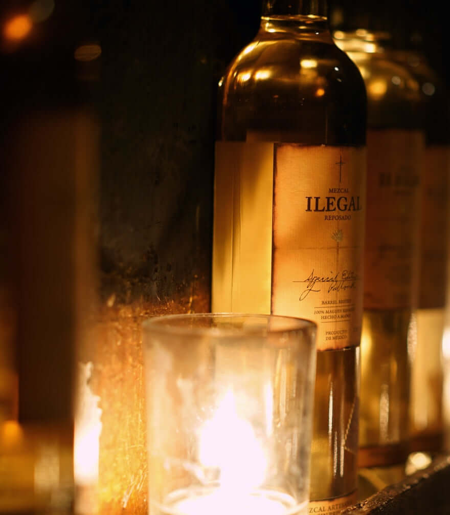 Ilegal Mezcal Reposado bottle illuminated by candlelight, showcasing its rich amber color and elegant label.