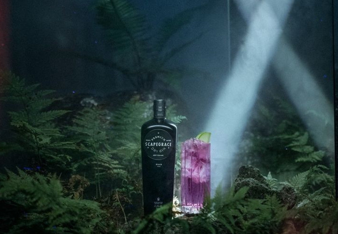 Scapegrace Dry Gin bottle with a cocktail in a lush setting, showcasing its unique New Zealand botanicals.