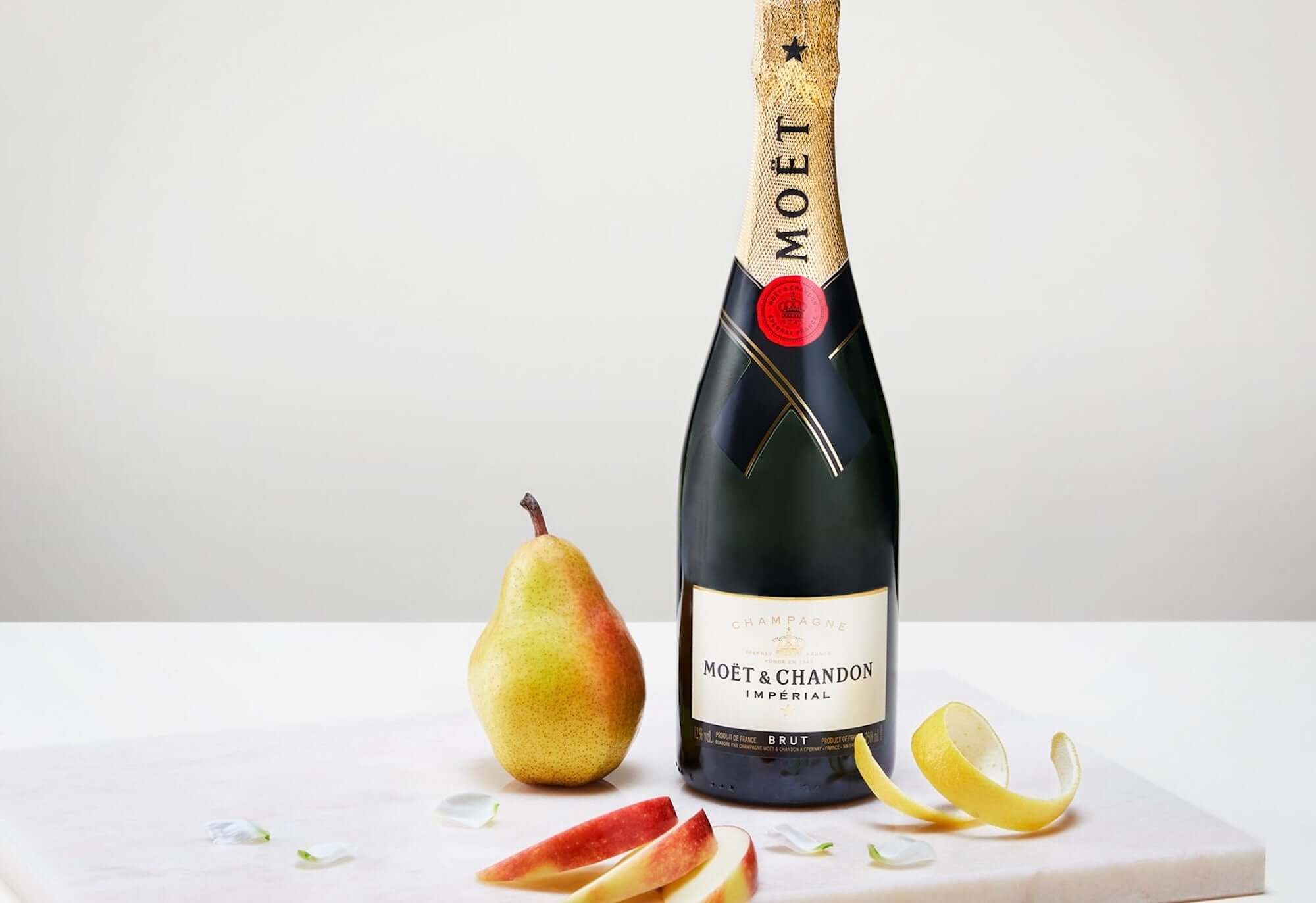Moët & Chandon Brut Impérial champagne bottle with a pear and apple peels on a white surface.