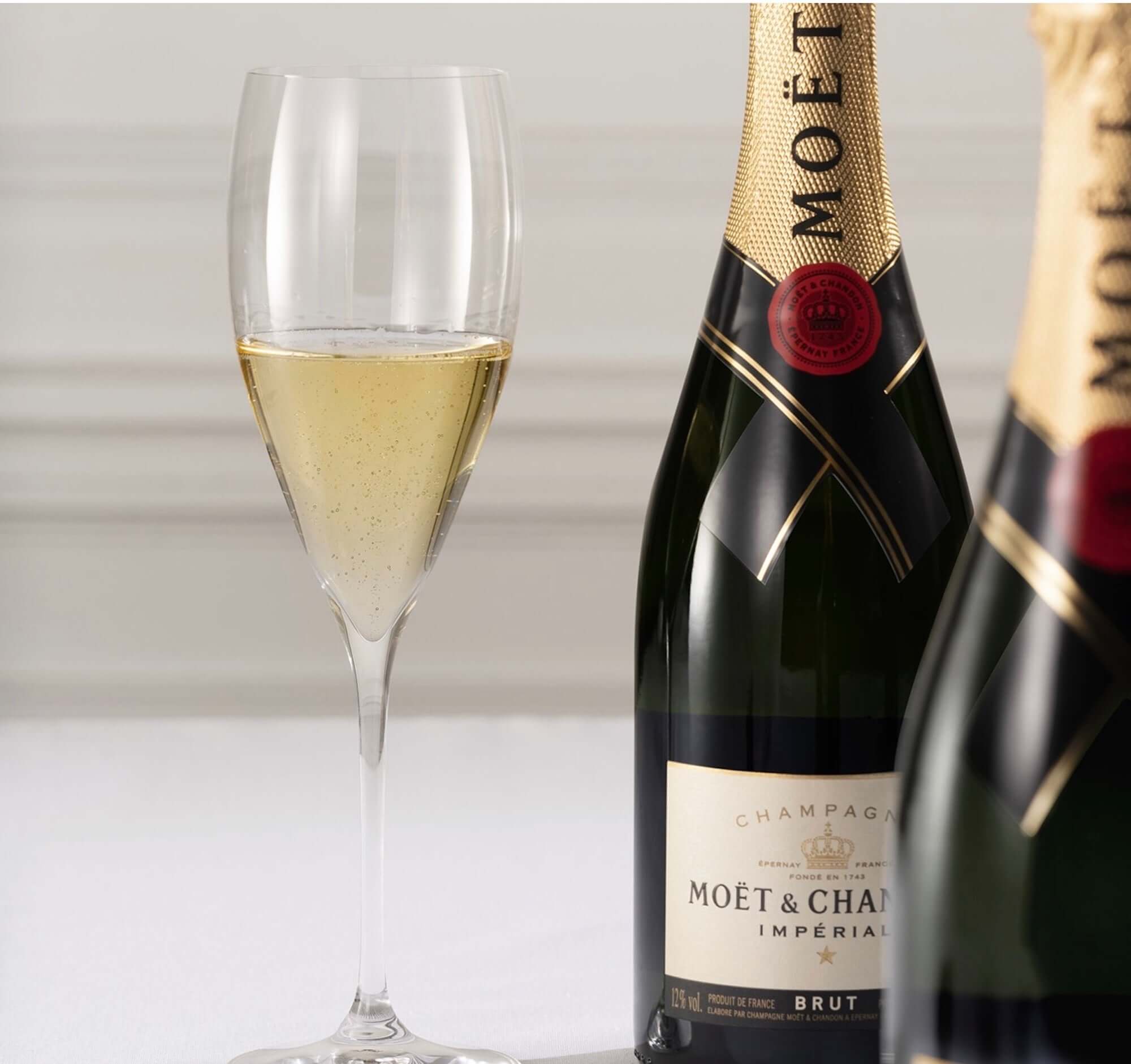 Moët & Chandon Brut Impérial champagne bottle and glass with sparkling wine on a white table.