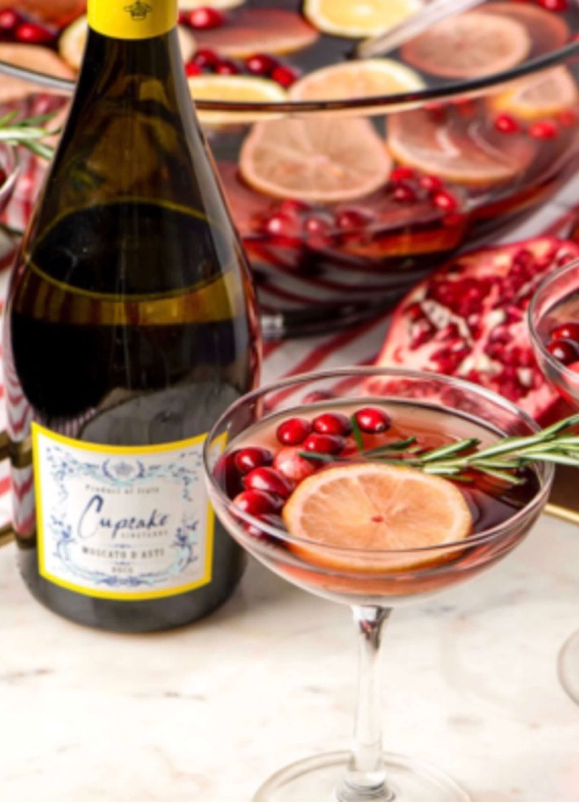 Cupcake Vineyards Moscato d'Asti bottle with festive cocktails topped with cranberries and lemon slices.