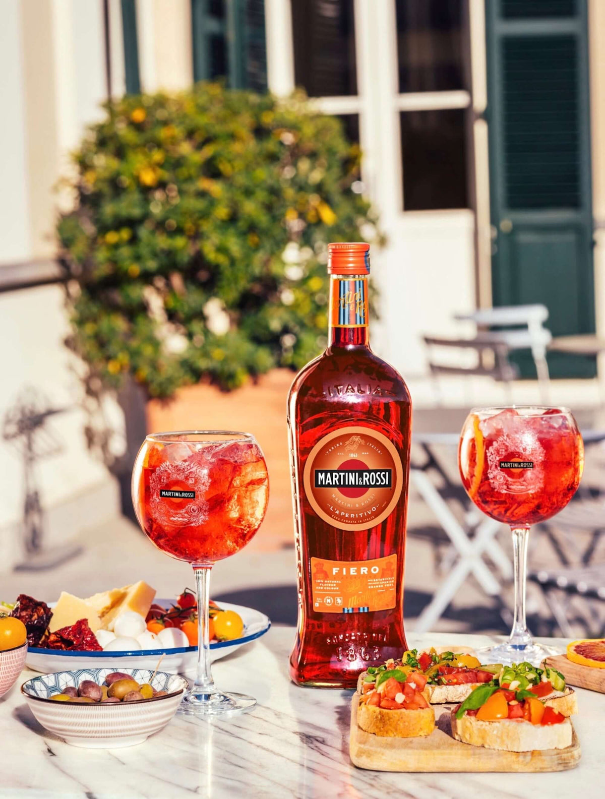 Martini and Rossi Fiero Vermouth bottle with cocktails and appetizers in a sunny outdoor setting.