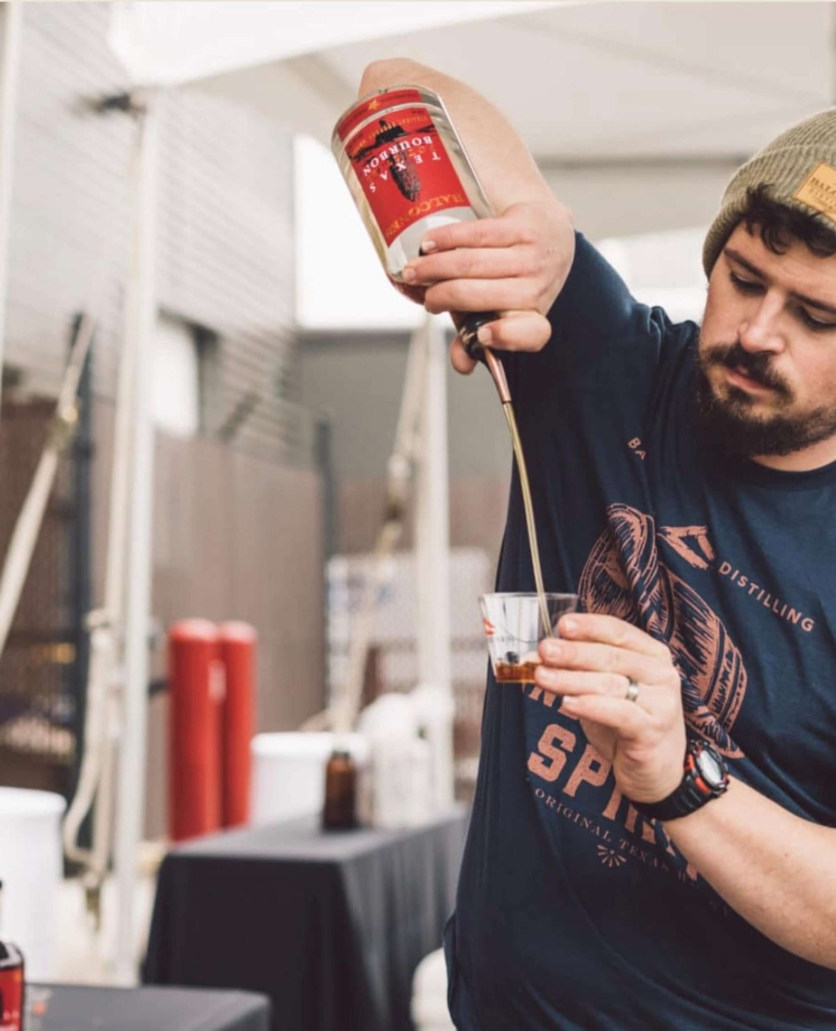 Man pouring Balcones Texas Pot Still Bourbon into a glass outdoors at a tasting event.