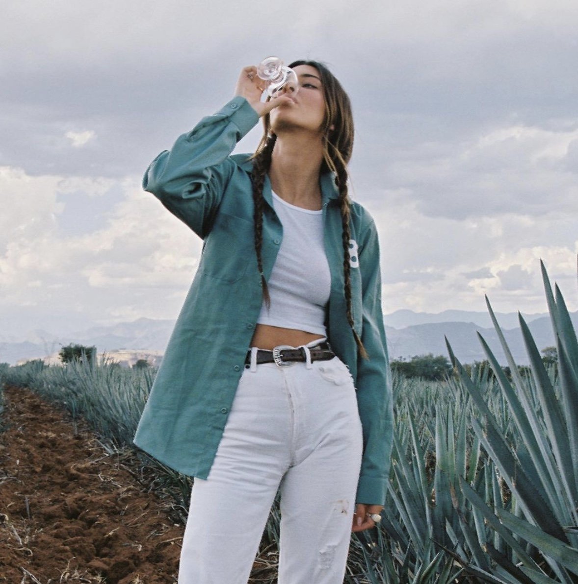 Person enjoying 818 Tequila in an agave field, promoting quality spirits and a connection to Mexican heritage.