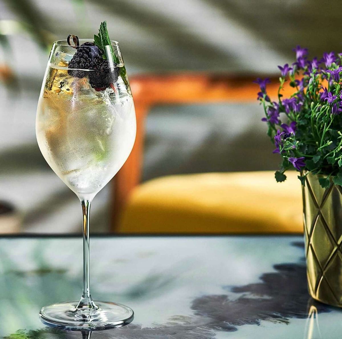 Refreshing blackberry cocktail in a stylish glass, garnished with mint, served on a table with flowers.
